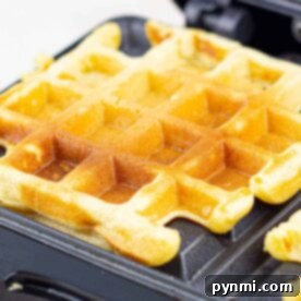 Golden and Crispy Cornmeal Waffles 9 Close-up of a golden cornmeal waffle cooking in a waffle maker, with crisp edges and the classic square pattern clearly visible.
