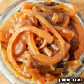 A jar filled with rich, slow cooker caramelized onions rests invitingly on a rustic wooden board.