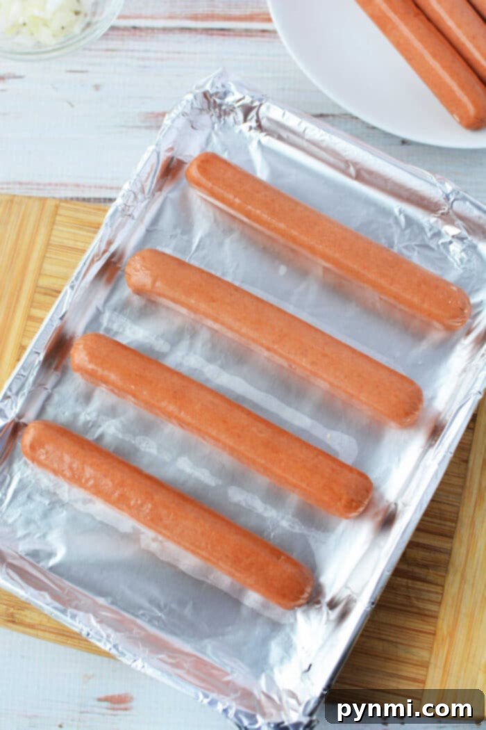 Detailed view of hot dogs cooking in the oven on a sheet pan, showing their plump texture.