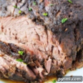 Perfect Fork-Tender Oven Brisket 7 Close-up of a seasoned, sliced roast beef on a white plate, reminiscent of how to make fall-apart brisket in the oven, garnished with chopped herbs.
