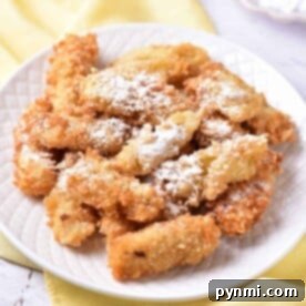 A plate of crispy banana tempura dusted with powdered sugar sits elegantly on a white plate atop a yellow cloth.