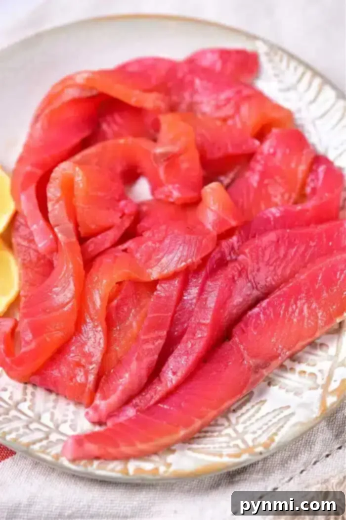 Slices of cured salmon are artfully arranged on a white plate with lemon wedges on the side, offering a perfect presentation to showcase your skills in mastering how to cure salmon.