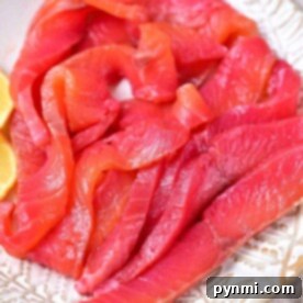 Slices of raw salmon rest elegantly on a patterned plate, accompanied by lemon wedges. Discover how to cure salmon for an enhanced flavor experience.