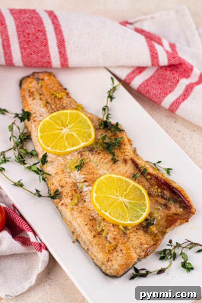 A complete plate of baked trout, lemon, and a side dish