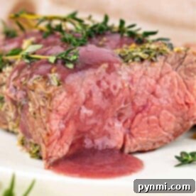 A juicy, medium-rare bottom round roast beef steak topped with herbs and red sauce on a white plate.