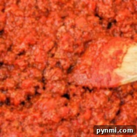 Close-up of a rich, chunky tomato sauce with cherry tomatoes, as a wooden spoon stirs the vibrant red mixture.