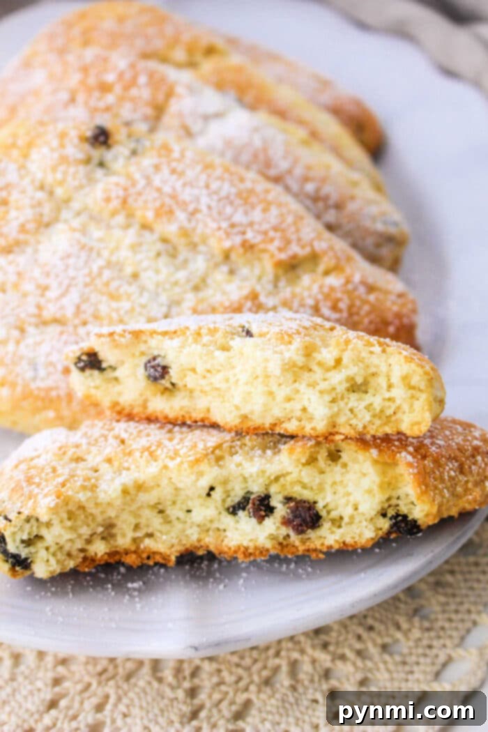 Two fluffy raisin scones, one cut in half to reveal its tender interior and plump raisins, served on a white plate with a golden spoon. The presentation highlights a delicious and comforting treat.