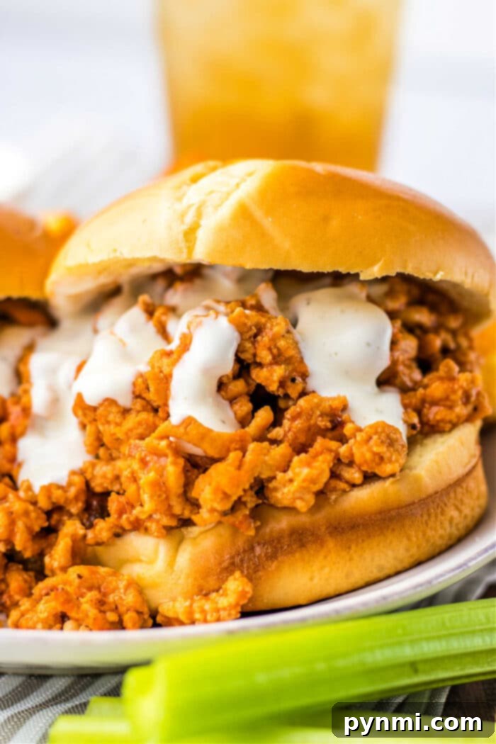 Close-up of ground chicken sloppy joe sandwich with creamy sauce on a bun, next to a few celery sticks.