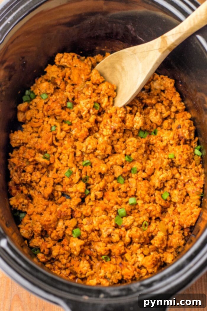 Cooked seasoned ground turkey in a crockpot with a wooden spoon, transforming it into a delightful dish reminiscent of Ground Chicken Sloppy Joes, garnished with chopped green onions.