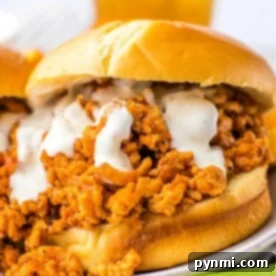 Close-up of slow cooker ground chicken sloppy joe sandwich with creamy sauce on a bun, next to a few celery sticks.