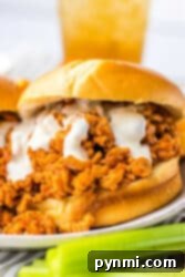 Close-up of slow cooker ground chicken sloppy joe sandwich with creamy sauce on a bun, next to a few celery sticks.
