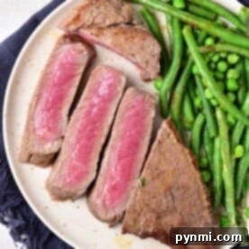 Sliced medium-rare chuck steak with green beans and peas on a white plate, resting on a dark napkin.