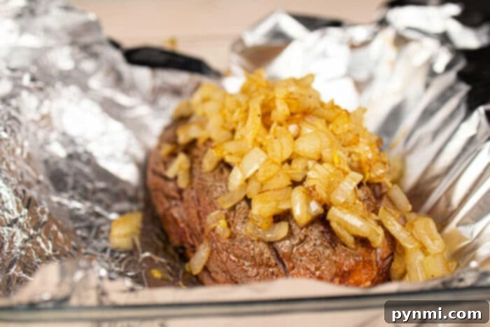Chuck roll steak topped with onions, resting on foil