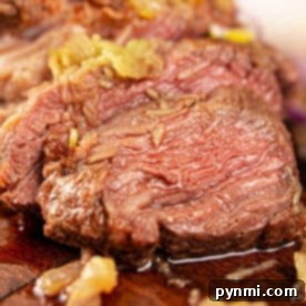 Close-up of juicy, sliced chuck roll steak topped with onions on a wooden cutting board.