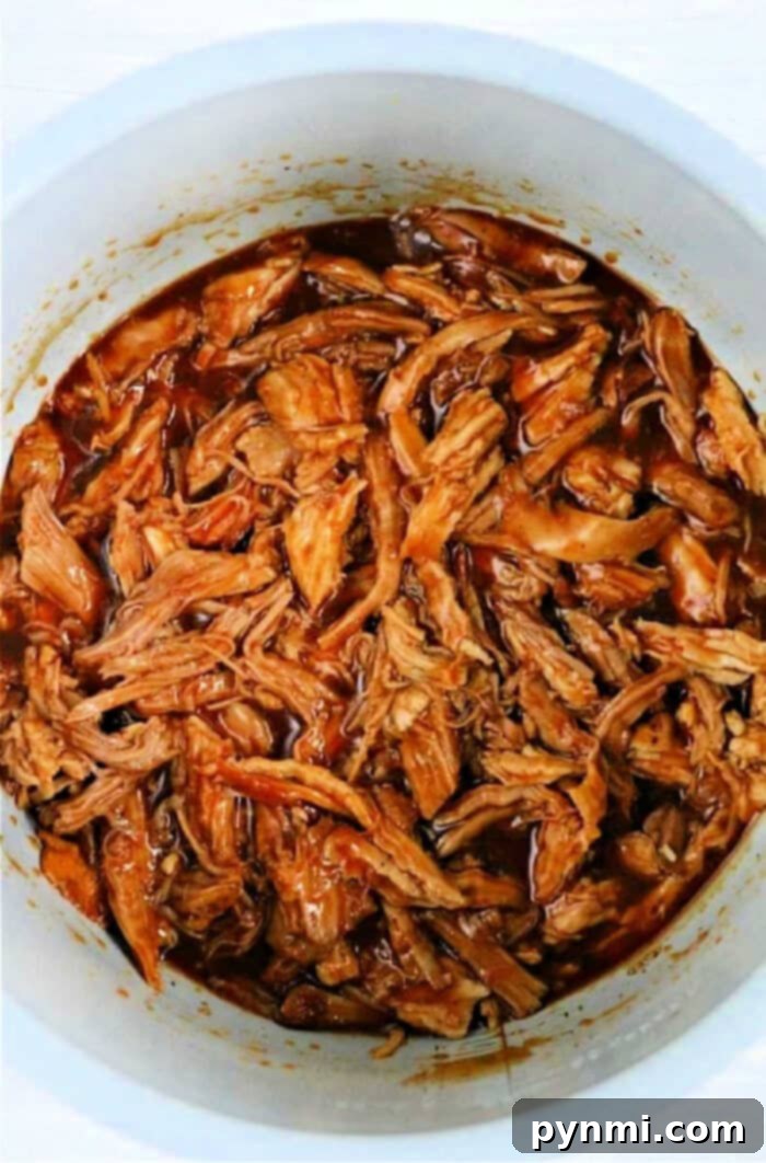 Your Leftover Pork Loin, Reimagined 4 A close-up of shredded barbecue pork in a white pot, covered in rich, dark sauce, promising delightful leftover pork loin recipes.