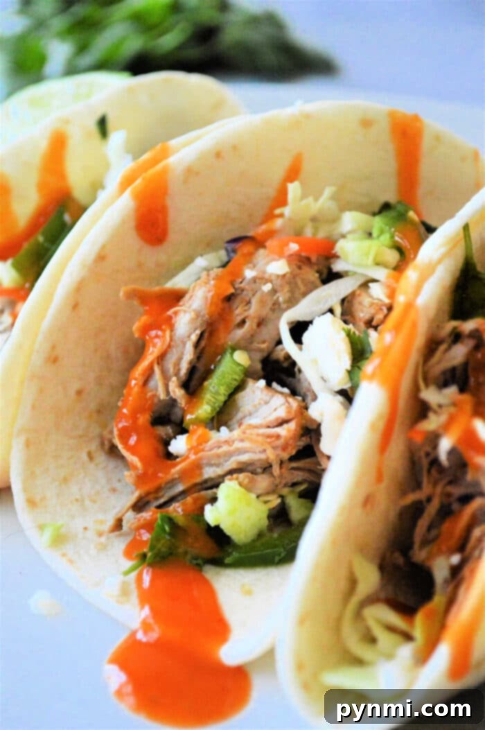 Your Leftover Pork Loin, Reimagined 5 A close-up of soft tacos filled with shredded pork and garnished with fresh toppings and a vibrant orange sauce.