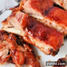 Close-up of glazed, barbecued ribs on a white plate with a fork, showcasing the perfect leftover ribs recipe for chili.