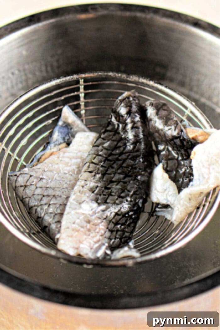Golden Fish Skin Cracklings 6 Gently placing blanched and dried fish skins into a wire strainer over a metal pot filled with hot oil, preparing for deep frying.