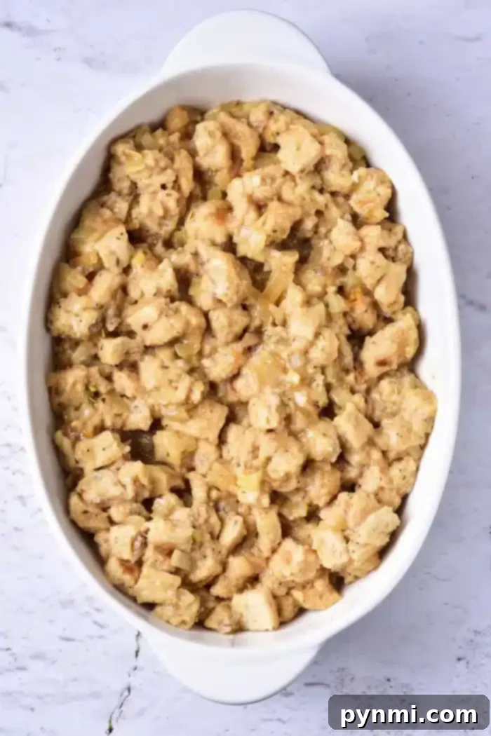 An elegant white oval casserole dish brimming with perfectly baked bread stuffing, featuring visible bread cubes, aromatic herbs, and savory onions, resting on a polished marble surface, ready to be served.