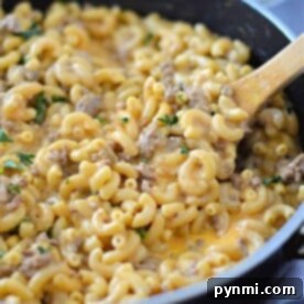 Creamy Velveeta Beef and Pasta Skillet 6 Macaroni and cheese with ground meat in a skillet, topped with herbs and stirred with a wooden spoon.
