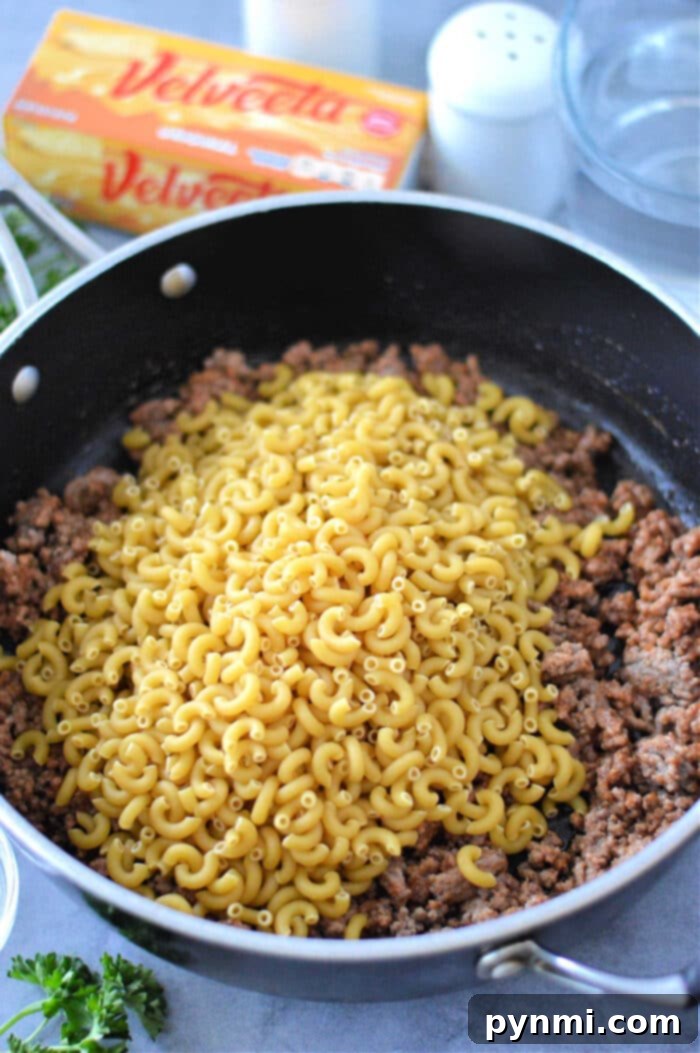 Creamy Velveeta Beef and Pasta Skillet 7 Homemade Cheeseburger Helper Recipe in a skillet, garnished with fresh herbs