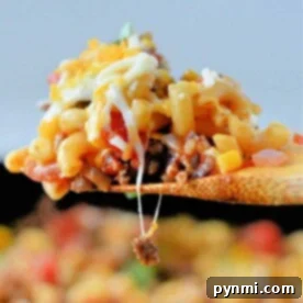 A close-up of a wooden spoon lifting cheesy, taco-flavored Hamburger Helper pasta with ground meat and vegetables.
