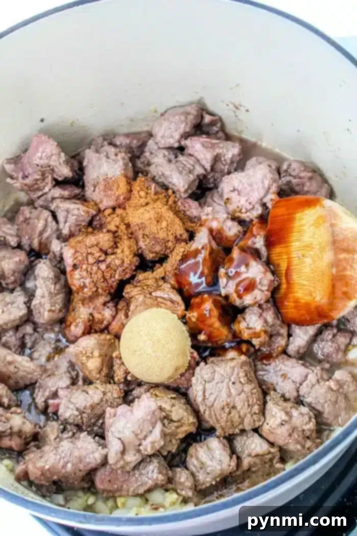 Slow-Braised Beef Bites 8 A pot containing braised beef tips cooked with spices, brown sugar, and a savory sauce. A wooden spoon is partially visible, resting on the edge of the pot.