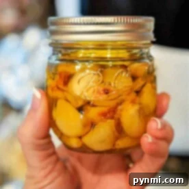 Whip Up Your Own Garlic Oil 6 A hand holds a glass jar filled with fragrant garlic cloves immersed in rich garlic oil.
