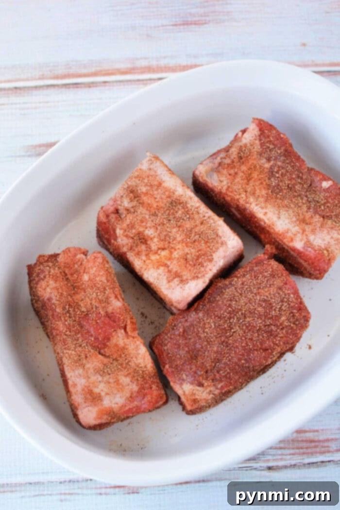Fall-Off-The-Bone Oven Beef Ribs 6 Tender seasoned beef ribs in a white dish on a light wooden surface, ready to be served after oven baking at 275 degrees.