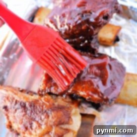 Coating beef ribs in a rich sauce with a red brush on a foil-lined tray, preparing them for slow roasting in the oven at 275.