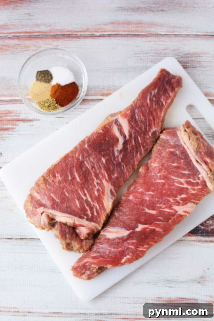 Two raw tri-tip steaks sit on a cutting board alongside a bowl of spices, ready to transform into a mouthwatering dish. Perfect for enthusiasts figuring out how to cook tri-tip in the oven, this setup promises savory success on any wooden surface.