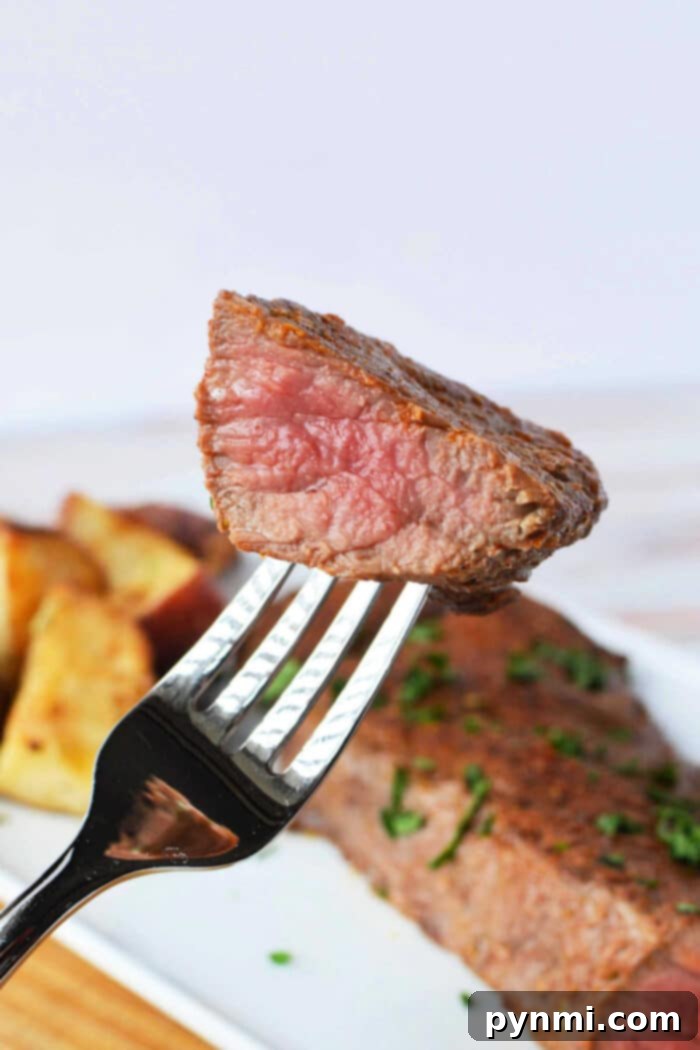 A fork holds a piece of juicy, medium-rare tri-tip steak above a plate featuring steak and roasted potatoes. For those wondering how to cook tri-tip in the oven, this succulent meal showcases the perfect harmony of tender meat and crispy sides.