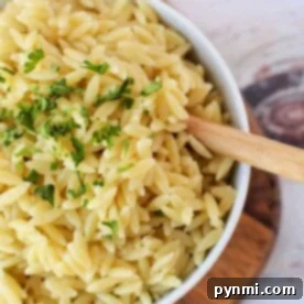 A bowl of perfectly cooked orzo pasta garnished with fresh parsley rests on a wooden board, accompanied by a rustic wooden spoon. Curious about crafting this dish? Discover how to cook orzo effortlessly to enjoy at home.
