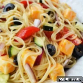 A delightful 4 Ingredient Pasta Salad featuring a plate of spaghetti salad with cheese cubes, sliced olives, tomatoes, red onions, and cucumbers.