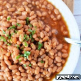 A white bowl filled with oven-baked beans, perfectly cooked at 350 degrees, is topped with chopped parsley and placed on a rustic wooden surface.