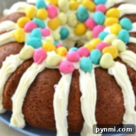 Easter Bundt Cake with white icing and colorful candy-coated eggs on top, artfully displayed on a blue plate.