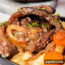 A plate of slow cooker osso buco with tender beef, accompanied by carrots and mashed potatoes, garnished with fragrant herbs.
