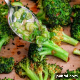 Asian-inspired roasted broccoli on a tray with a spoonful of savory dressing being drizzled over it.
