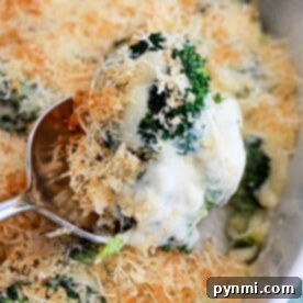Close-up of a spoon lifting creamy Broccoli Au Gratin with breadcrumbs and cheese from a dish.