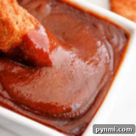 Chicken tender being dipped into a rich, homemade Popeyes barbecue sauce in a white bowl, close-up shot
