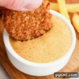A hand dips a chicken nugget into creamy dipping sauce, reminiscent of those signature flavors youd find when learning how to make Burger King sauces, with crispy fries in the background on a wooden board.