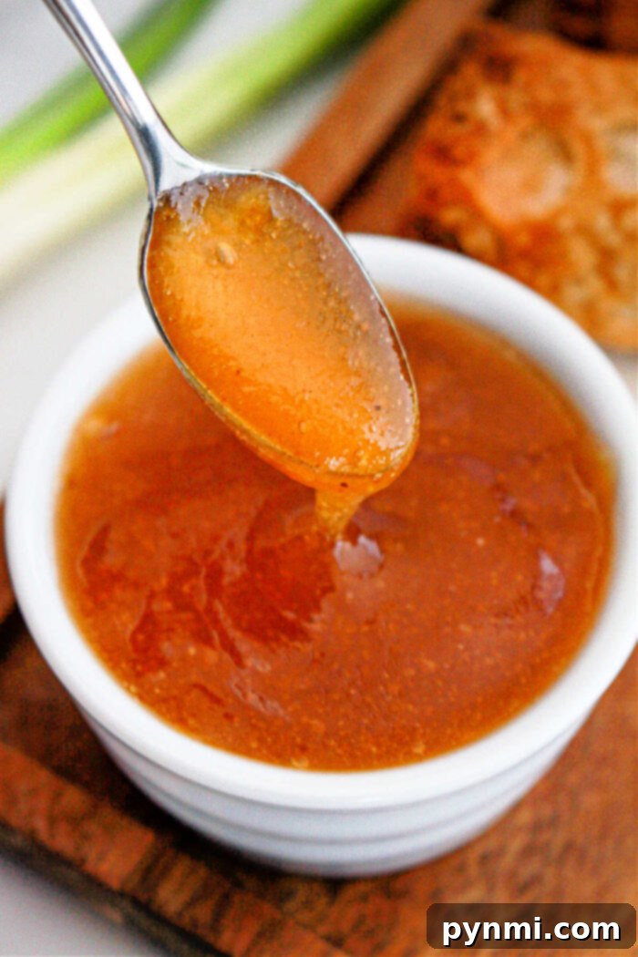 A crispy egg roll is carefully dipped into a bowl of homemade dipping sauce, highlighting its golden exterior.