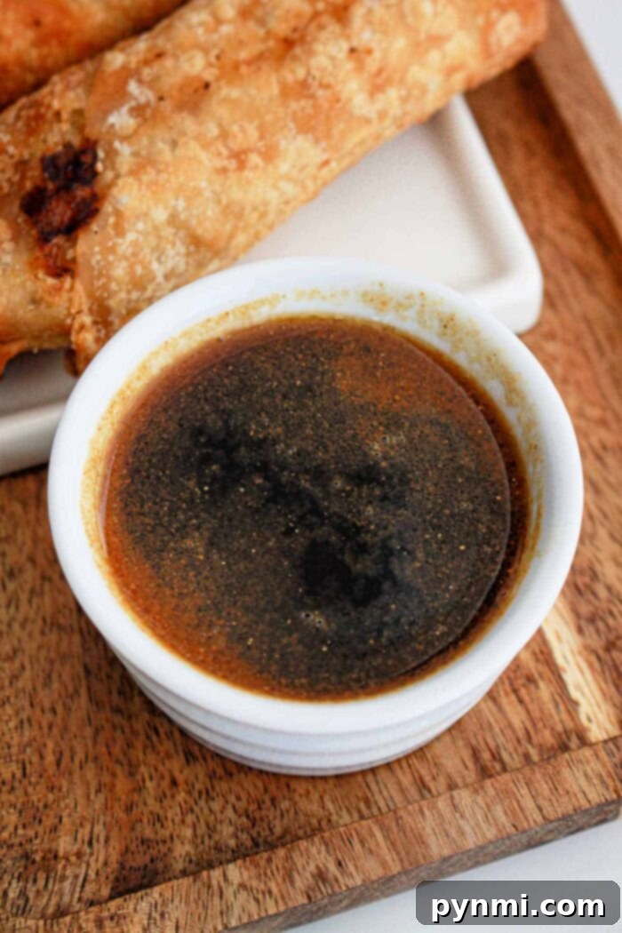 A close-up of a bowl filled with savory Soy-Based Egg Roll Sauce, garnished lightly.