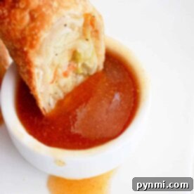 An egg roll gracefully meets its match as its dipped into a small white bowl brimming with rich egg roll sauce, all set on a pristine white plate.