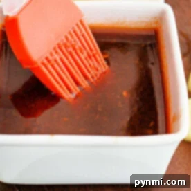 A square white dish holding Huli Huli Sauce, complemented by an orange basting brush resting inside.