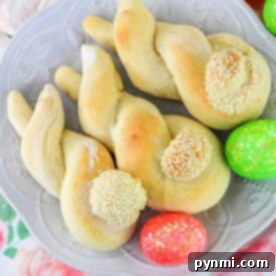 Twisted bread rolls with sesame seeds sit on a plate, surrounded by brightly colored Easter eggs, reminiscent of a delightful bunny bread recipe perfect for celebrating the spring season.