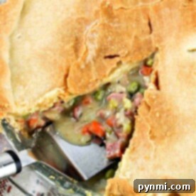 A golden-crusted Ham Pot Pie, with a slice removed to reveal a filling of ham, peas, carrots, and creamy sauce.