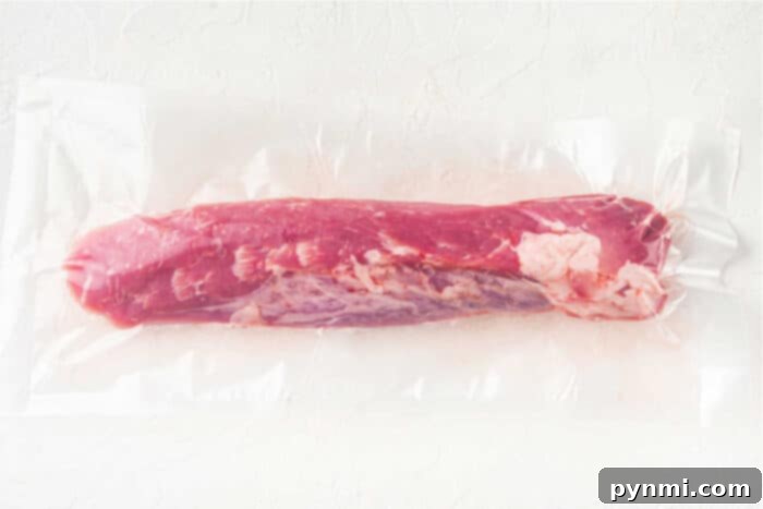 Mouthwatering Pork Tenderloin Tacos 3 A vacuum-sealed package containing a raw, whole pork tenderloin on a plain, light-colored surface. The meat is pink with visible marbling and fat along its side—perfect for making mouthwatering Pork Tenderloin Tacos.