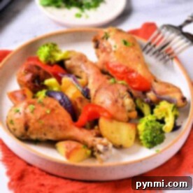 Plate of crispy roasted chicken drumsticks with mixed vegetables on an orange napkin, offering a delightful hint of how long to cook chicken legs in the air fryer for that perfect crunch.