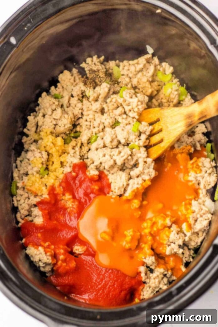 Mix ground chicken, diced peppers, and sauces in a slow cooker with a wooden spoon, perfect for those considering versatile ground chicken recipes.